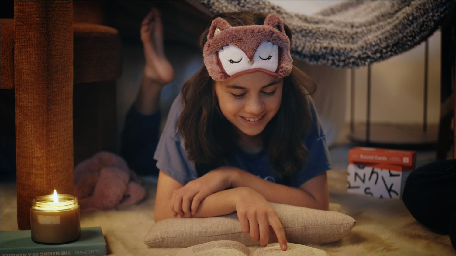 girl lays in a blanket fort reading and smiling with a candle a book and her Phonics Sound Cards by Aansen Literacy