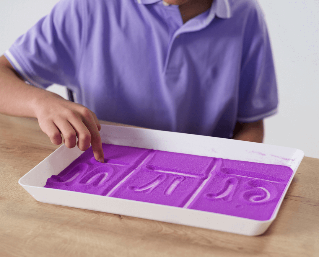 Boy writes letters in a purple sand tray
